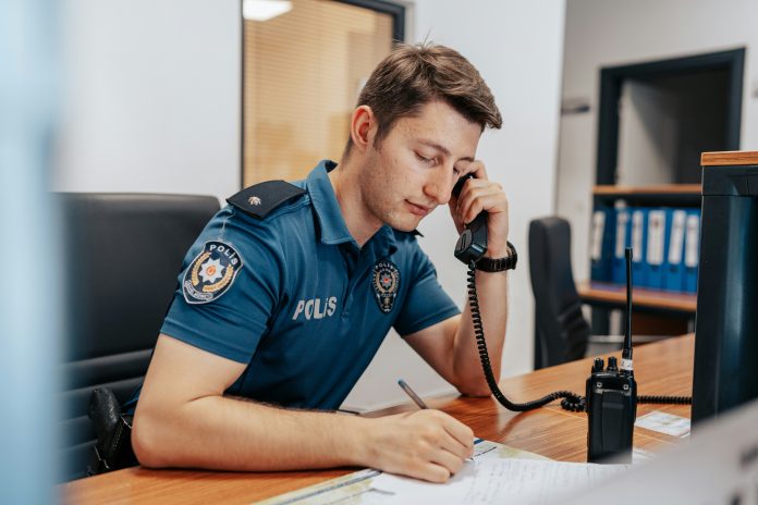 ahmet-kurt-kcRAcGBy8WU-unsplash a police officer sitting at his desk in uniform, answering a call.