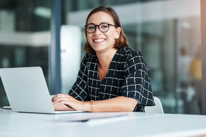 Portrait,,Woman,And,Typing,In,Office,With,Laptop,For,Work woman sitting at a desk with her computer.